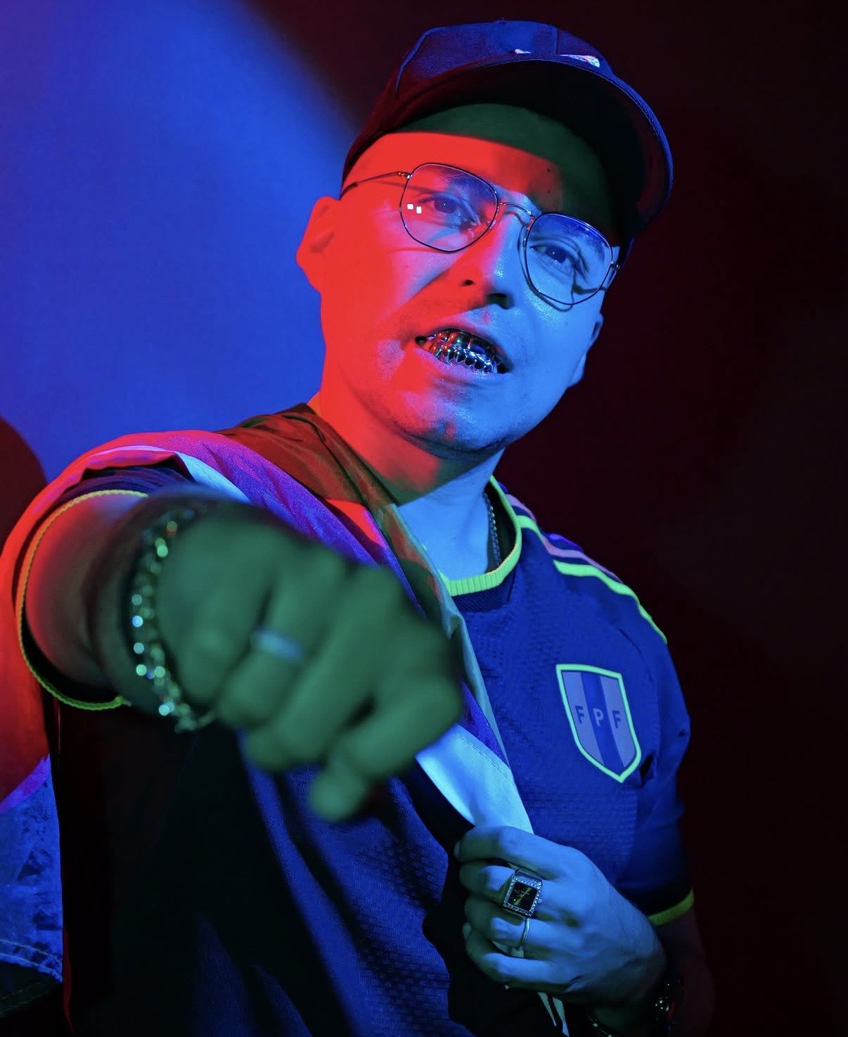 Alejo Opiano wearing glasses and a cap under red and blue lighting